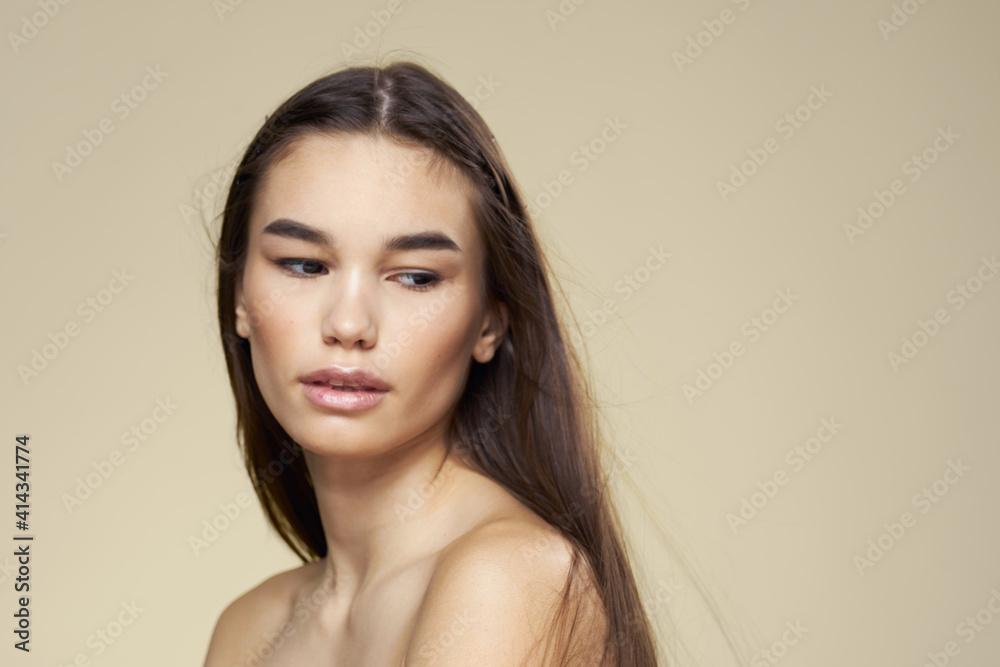 Brunette with bare shoulders close-up long hair beige background clean skin Brunette with bare shoulders close-up long hair beige background clean skin