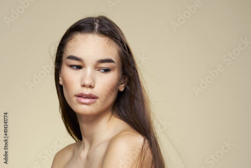 Brunette with bare shoulders close-up long hair beige background clean skin