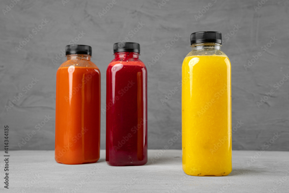 Three plastic bottles with freshly squeezed juice on gray background Three plastic bottles with freshly squeezed juice on gray background