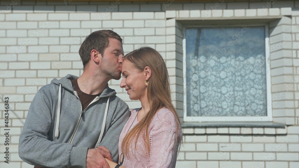 A loving husband kisses his wife in front of his house. A loving husband kisses his wife in front of his house.