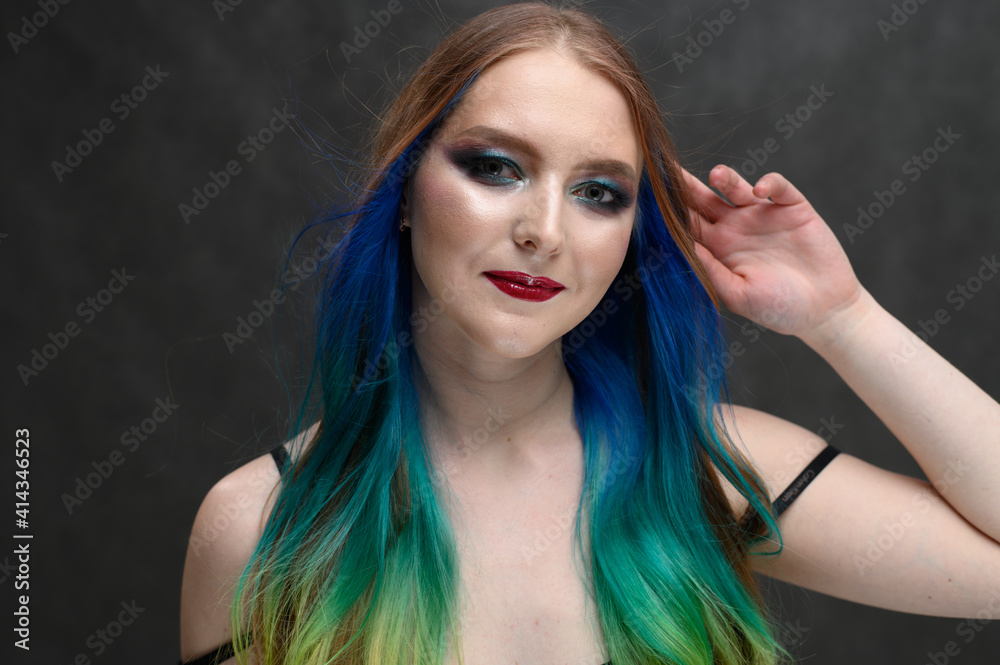 Fototapeta premium Portrait of caucasian young beautiful brunette woman with dyed hair and bright makeup smiling on a blurred gray background, close up