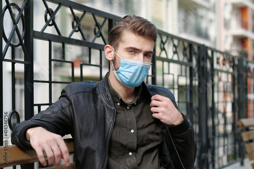 Handsome man in medical protective mask sits on bench and looks at camera