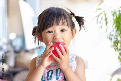 Portrait​ image​ of​ 2-3 yeas​ old​ of​ baby.​ Happy​ Asian child girl eating and biting an red apple. Enjoy eating moment. Healthy food and kid concept.​