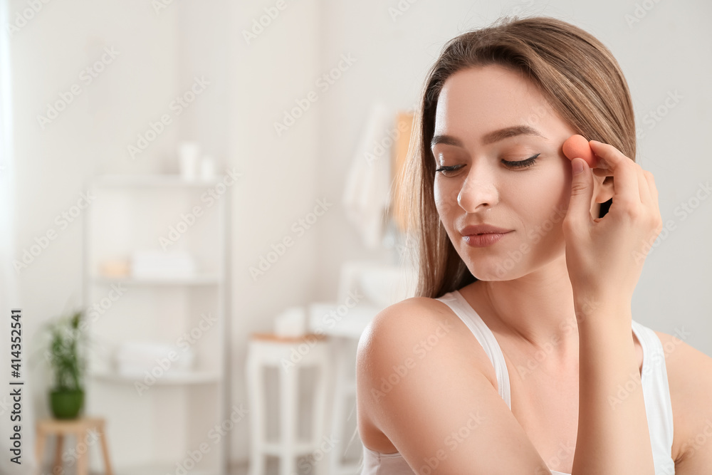 Beautiful young woman with sponge applying makeup at home Beautiful young woman with sponge applying makeup at home