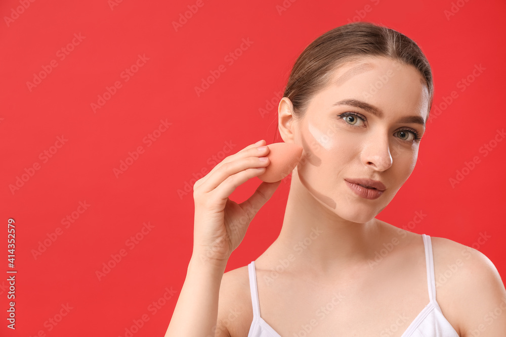 Beautiful young woman applying contouring makeup against color background