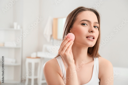 Beautiful young woman with sponge applying makeup at home