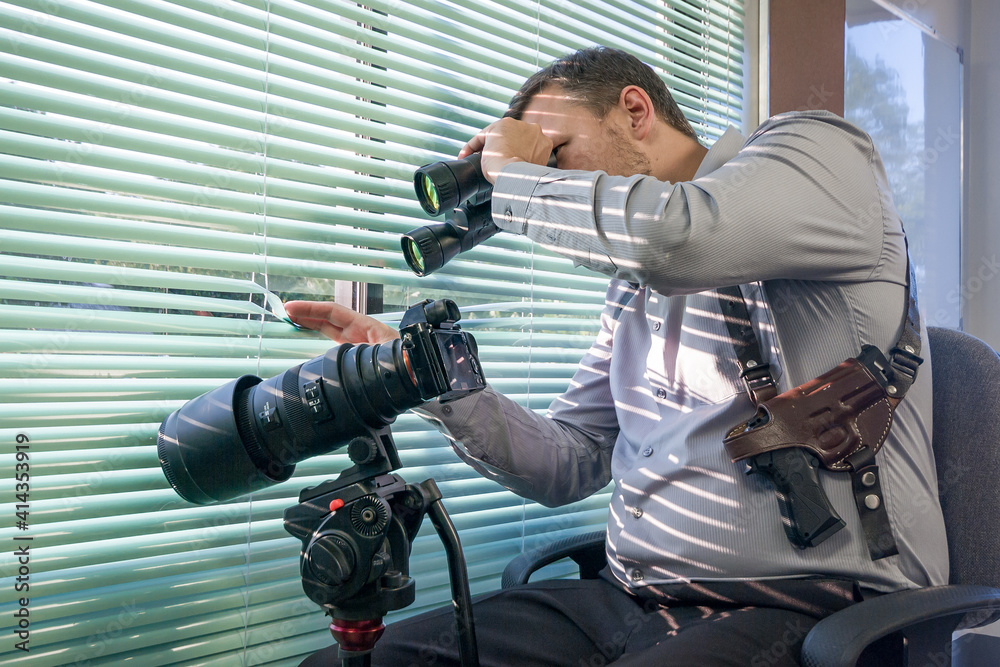 Obraz premium The agent is looking at the binoculars and sitting near the blinds