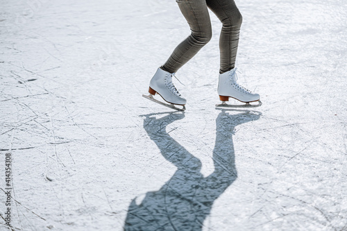 Young woman ice skating outdoors on a pond on a freezing winter day. Detail of skate shoes.