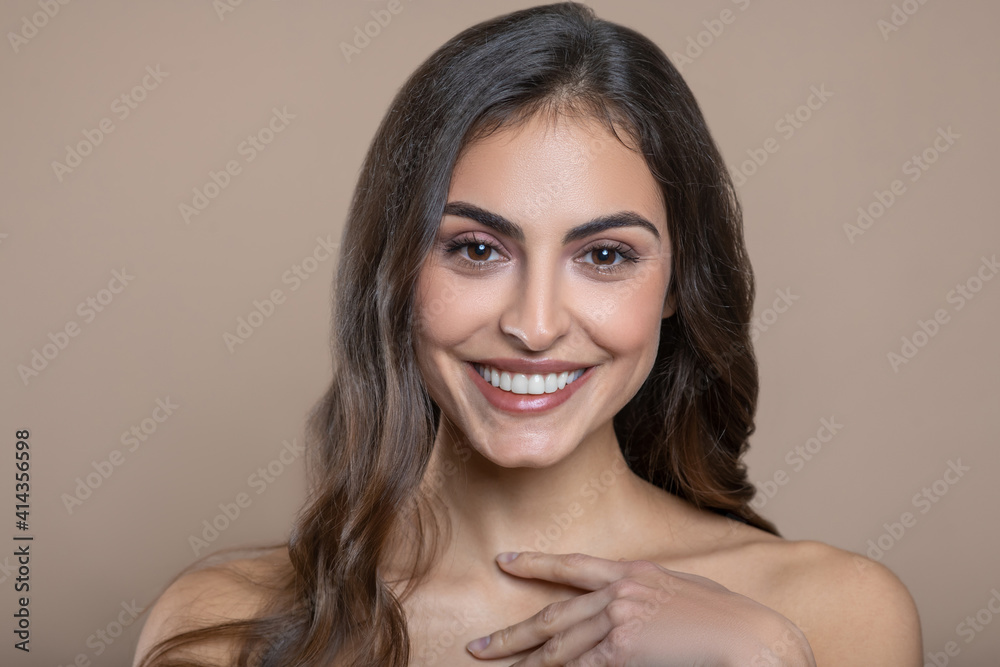 Fototapeta premium Joyful young woman touching with fingers near neck