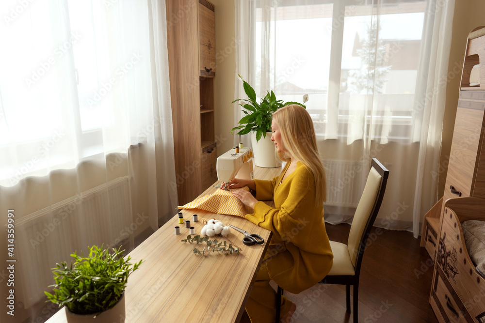 A woman sits at the sewing maching cutting a piece of cotton with the scissors A woman sits at the sewing maching cutting a piece of cotton with the scissors