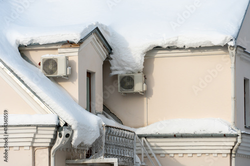 The roofs of the buildings are covered with snow and ice after a big snowfall. External split wall air conditioner compressor unit installed on the outside of the building.