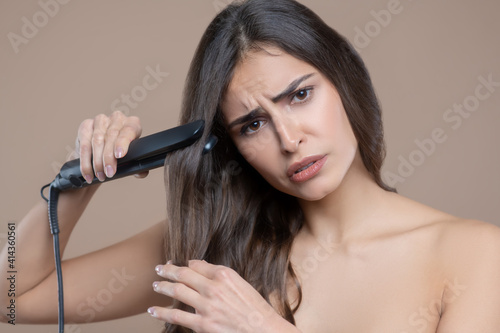 Sad woman with bare shoulders and hair straightener