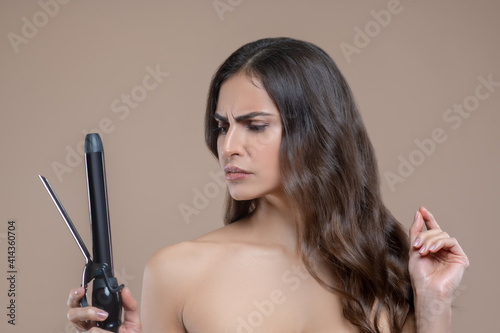 Woman sternly looking at curling iron in hand