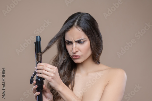 Serious woman winding her curl on curling iron