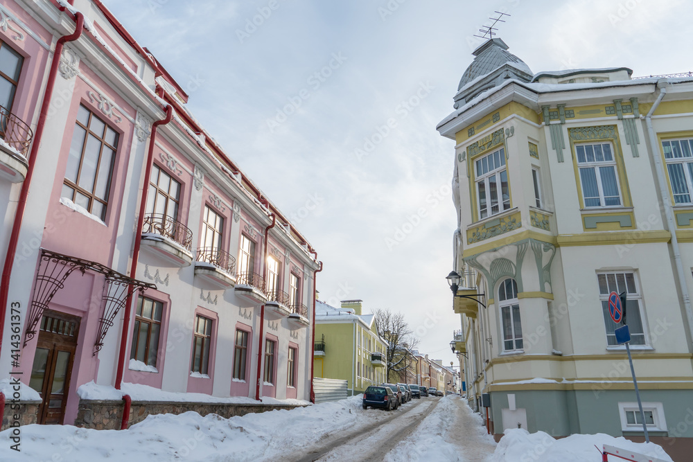 View of a narrow street covered with snow after a snowfall. The roadway is covered with snow and ice. Beautiful old houses in the historical center of the city