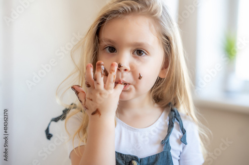 little blonde cute girl got her chocolate fingers dirty and licks them.