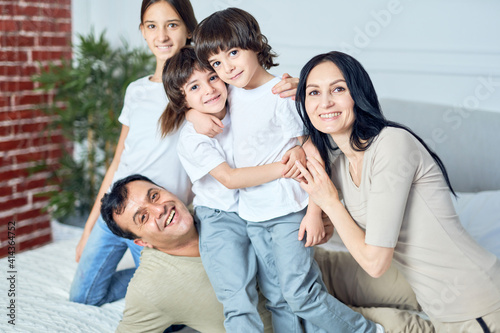 Family time. Portrait of happy latin family, parents and children smiling at camera while spending time together at home