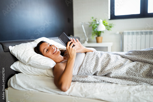 Happy woman lying on bed smiling while reading a text message