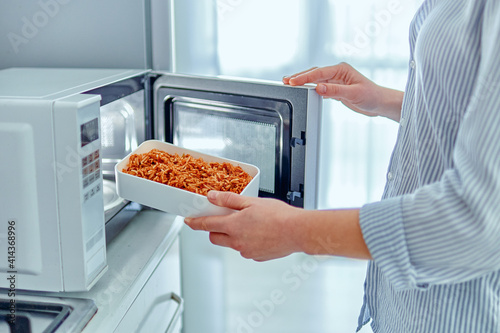 Female hands warming up a container of food in the modern microwave oven for snack lunch at home