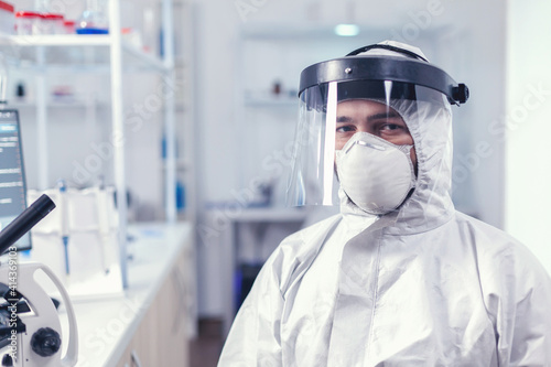 Fatigued medical scientist sitting at workplace wearing coverall with face mask against covid19 . Overworked researcher dressed in protective suit against invection with coronavirus during global photo