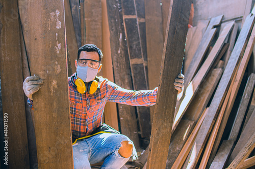 carpenter is working in a woodworking office.A white male carpenter is selecting the wood material and brushing off the sawdust.