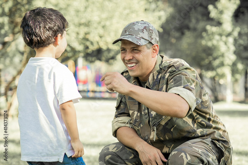 Happy military father meeting with son after mission trip. Boy walking to dad wearing camouflage uniform in park. Family reunion or returning home concept © Mangostar