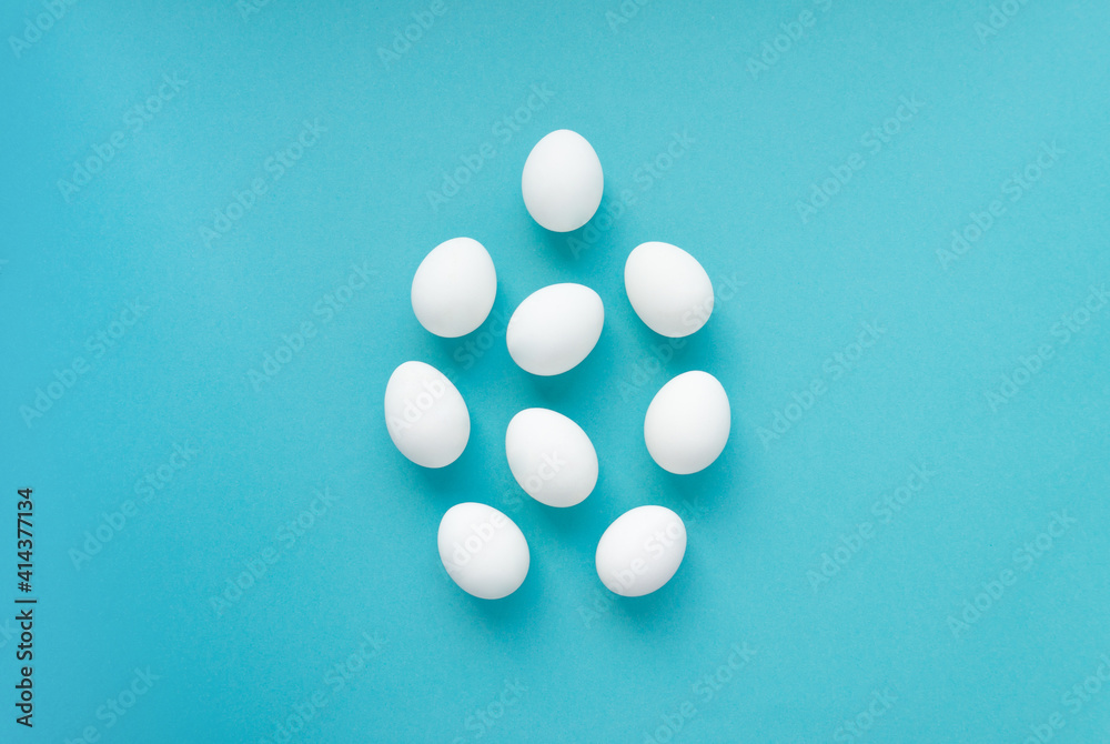 White chicken eggs are laid out in the shape of a large egg in the center of a blue background. Easter card, top view White chicken eggs are laid out in the shape of a large egg in the center of a blue background. Easter card, top view