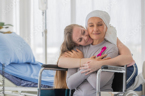 A middle-aged breast cancer woman with clothing around her head effected from chemo therapy sitting on wheel chair and hold hand of her daughter with hope and trust in love. photo