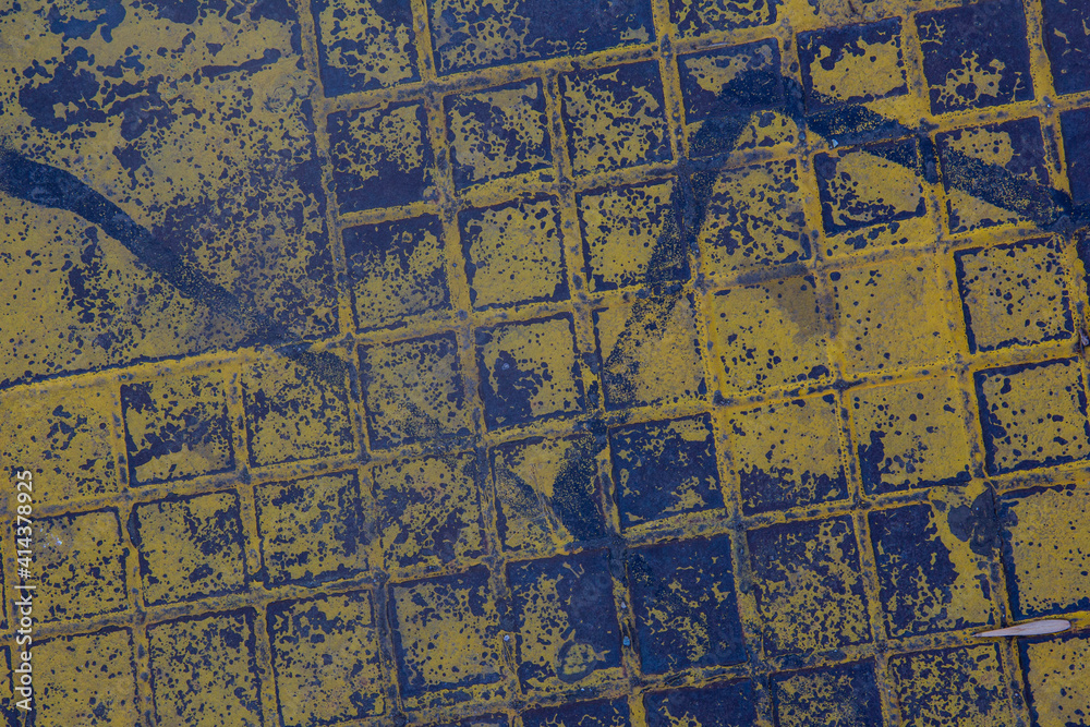 The texture of a manhole cover drenched in yellow paint.