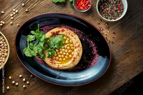 A classic oriental appetizer dish - chickpea hummus with white olive oil, served on a black plate on a wooden background. Restaurant food