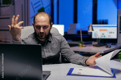 Entrepreneur trying to understand project sitting at his deks in empty office. Confused businessman while doing overtime to finish a big project for company. photo