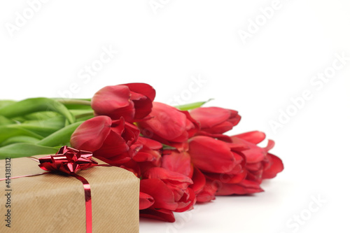 Spring banner composition from gift box  covered by brown craft paper  tied by red bow and ribbons  fresh red tulip flowers on white background isolated with copy space  selective focus