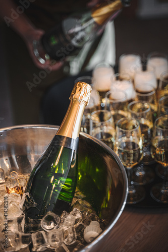 bottle of champagne in ice and person pouring glasses in the background