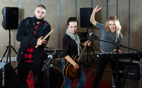 Expressive active group of rock musicians posing with instruments in recording studio
