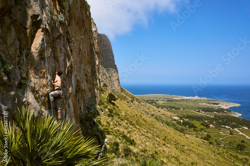 young caucasian man climbing on a limestone crag near San Vito lo Capo in Sicily with wide panoramic view 2