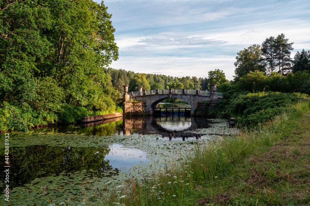Fototapeta premium View of the Slavyanka River and the Viscontiev Bridge in the Pavlovsk Palace and Park Complex on a summer day, Pavlovsk, Saint Petersburg, Russia