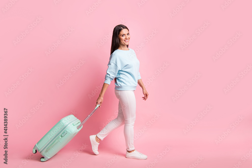 Full length body size photo of brunette going to airport terminal with baggage smiling isolated on pastel pink color background Full length body size photo of brunette going to airport terminal with baggage smiling isolated on pastel pink color background