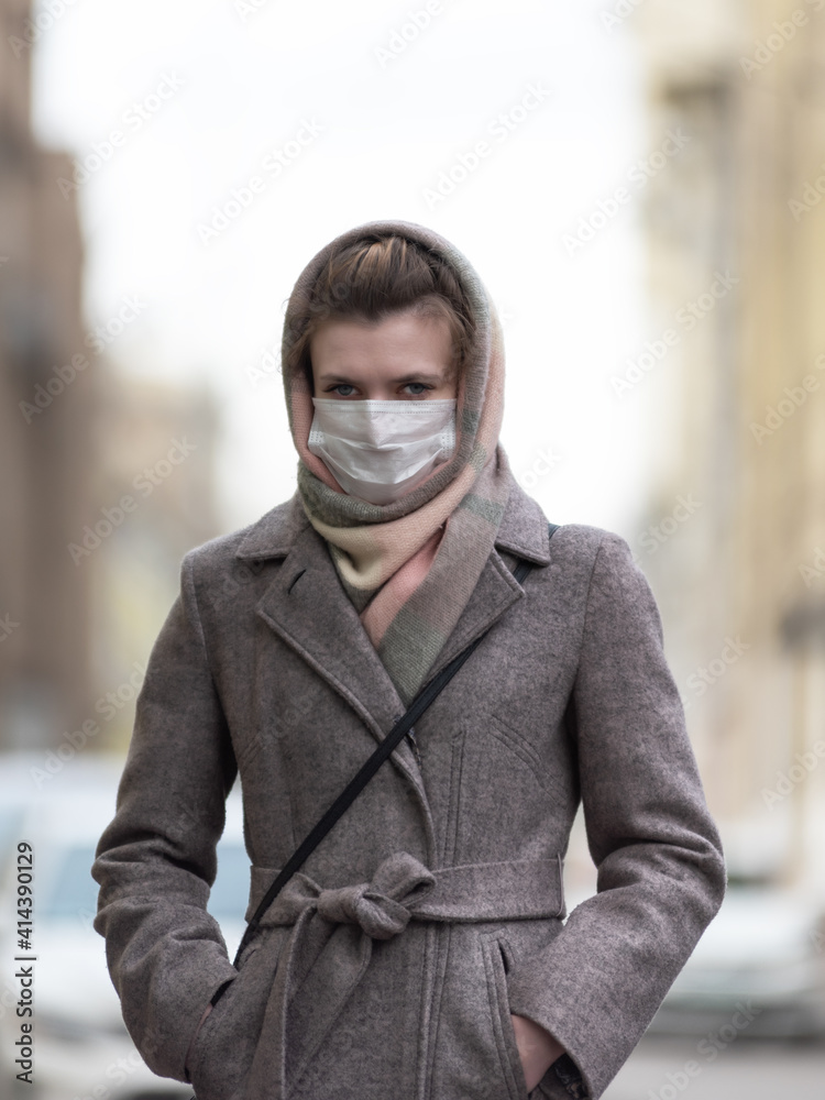 Young pretty woman in coat outdoors wearing medical mask