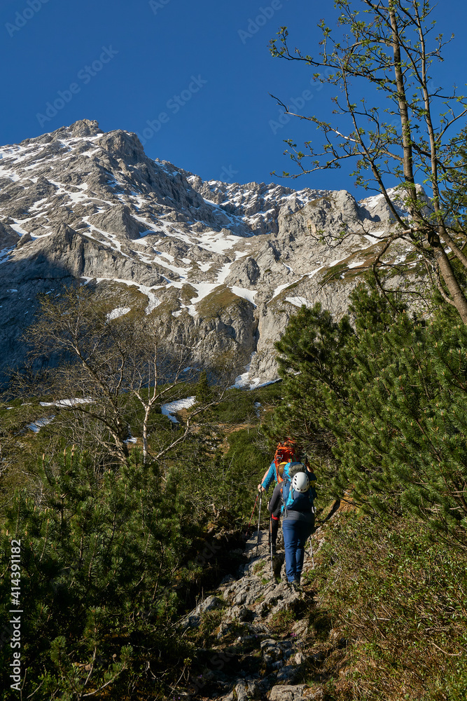 mountaineering woman hiking toward high peak in the distance on a lush green trail with full rucksack