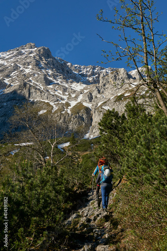 mountaineering woman hiking toward high peak in the distance on a lush green trail with full rucksack