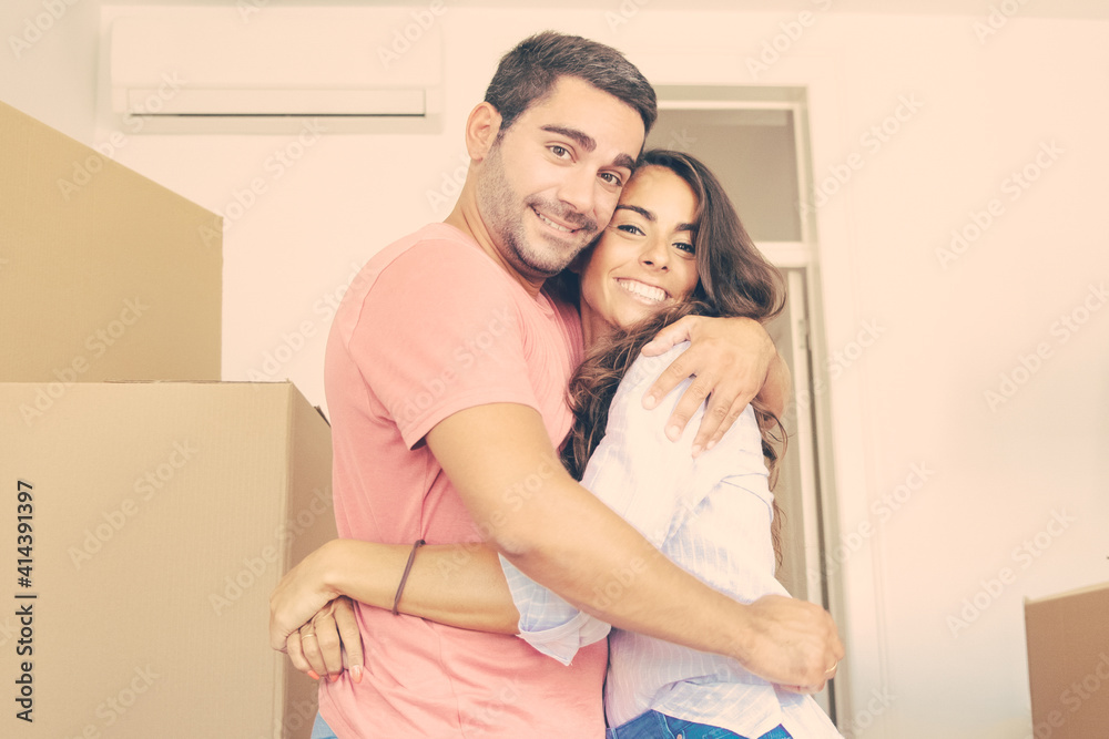 Happy couple moving into new apartment, standing among carton boxes and hugging. Medium shot. New home concept Happy couple moving into new apartment, standing among carton boxes and hugging. Medium shot. New home concept