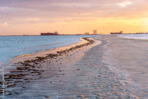 Canvas Print Ships at sea at sunset, viewed from a flat shoreline with ice on the sand with a