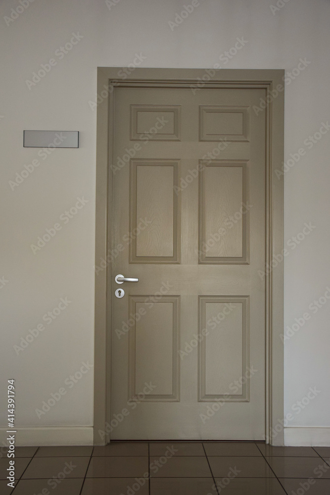 Closed light door of an office space with a blank sign on the left side on the wall