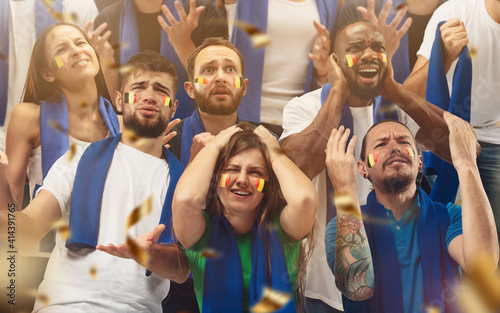 Belgian football, soccer fans cheering their team with a blue scarfs at stadium. Excited fans cheering a goal, supporting favourite players. Concept of sport, human emotions, entertainment.