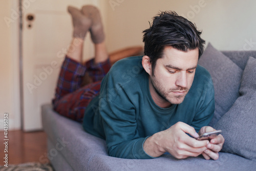 Young handsome man lying on a couch with smartphone wearing lyjamas © Надежда Филатова