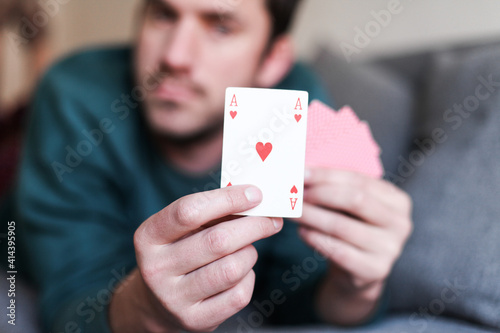 Man is holding an ace of hearts card, laying on a couch at home, playing cards at home 