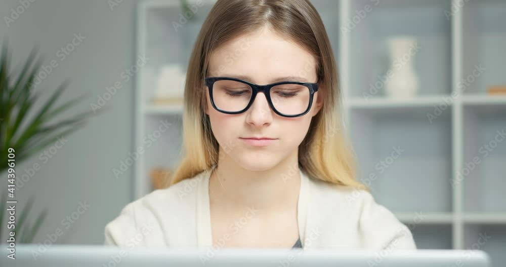 Closeup portrait of young woman working on laptop. Face of a student girl in glasses looks into the computer sitting in a stylish interior. Closeup portrait of young woman working on laptop. Face of a student girl in glasses looks into the computer sitting in a stylish interior.