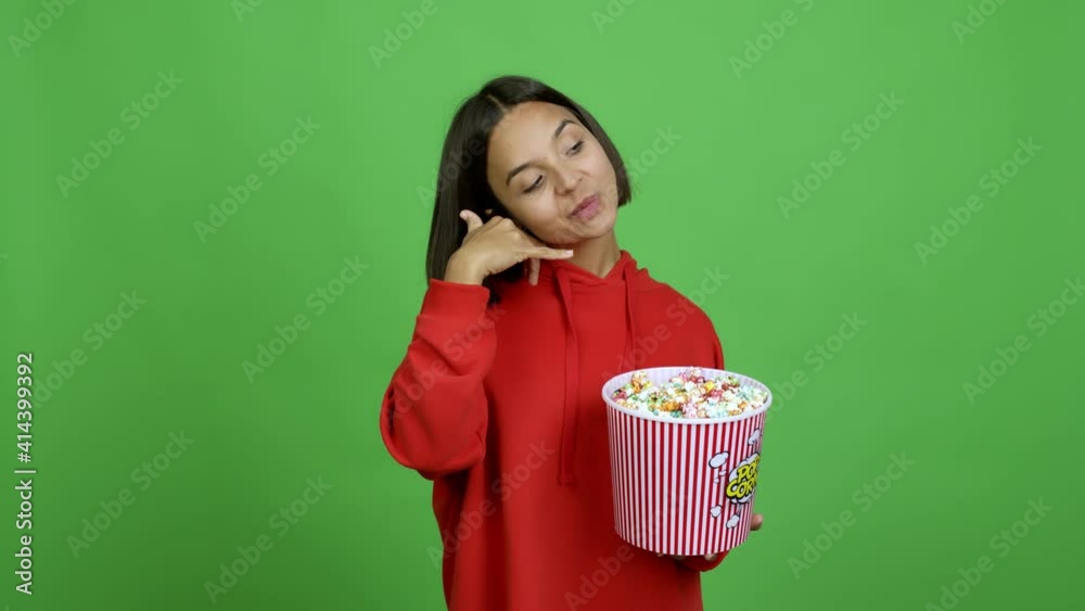 Woman holding a bowl of popcorns making phone gesture and speaking with someone. Call me back sign over isolated background Woman holding a bowl of popcorns making phone gesture and speaking with someone. Call me back sign over isolated background