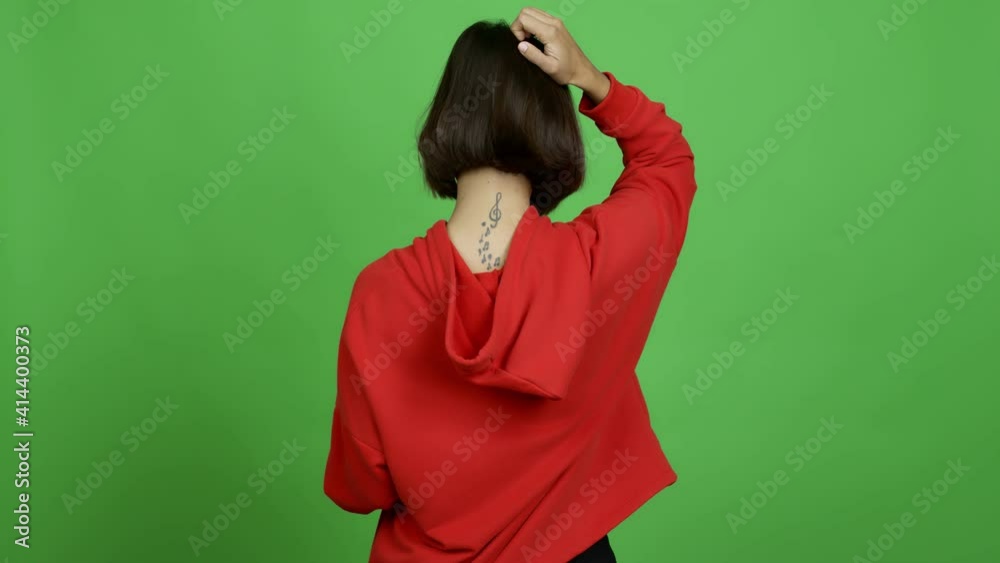 Woman holding a bowl of popcorns on back position looking back while scratching head over isolated background Woman holding a bowl of popcorns on back position looking back while scratching head over isolated background