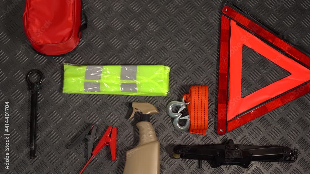 Closeup top view 4k stock video footage of many tools and equipment need for safe driving by car. Different objects laying on black rubber protective rug inside of boot of automobile. Emergency kit